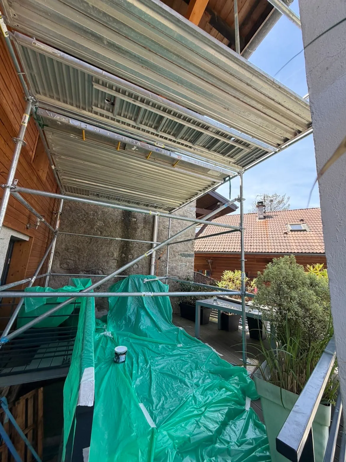 Échafaudage monté au-dessus d’une terrasse, sol et mobilier protégés par des bâches