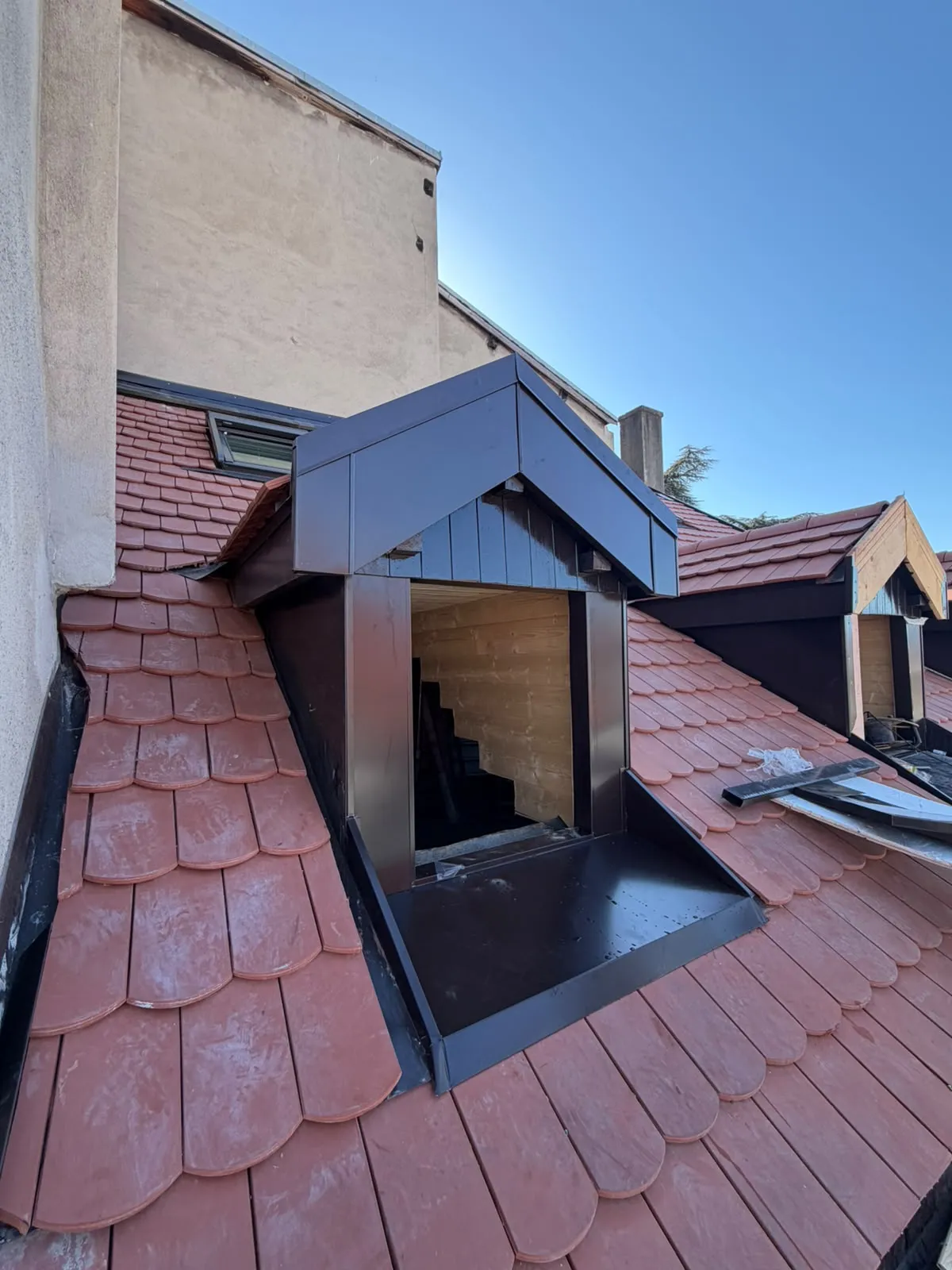 Lucarne entièrement habillée de tôle marron façonnée sur mesure, avec sa bavette, sur une toiture en tuiles plates
